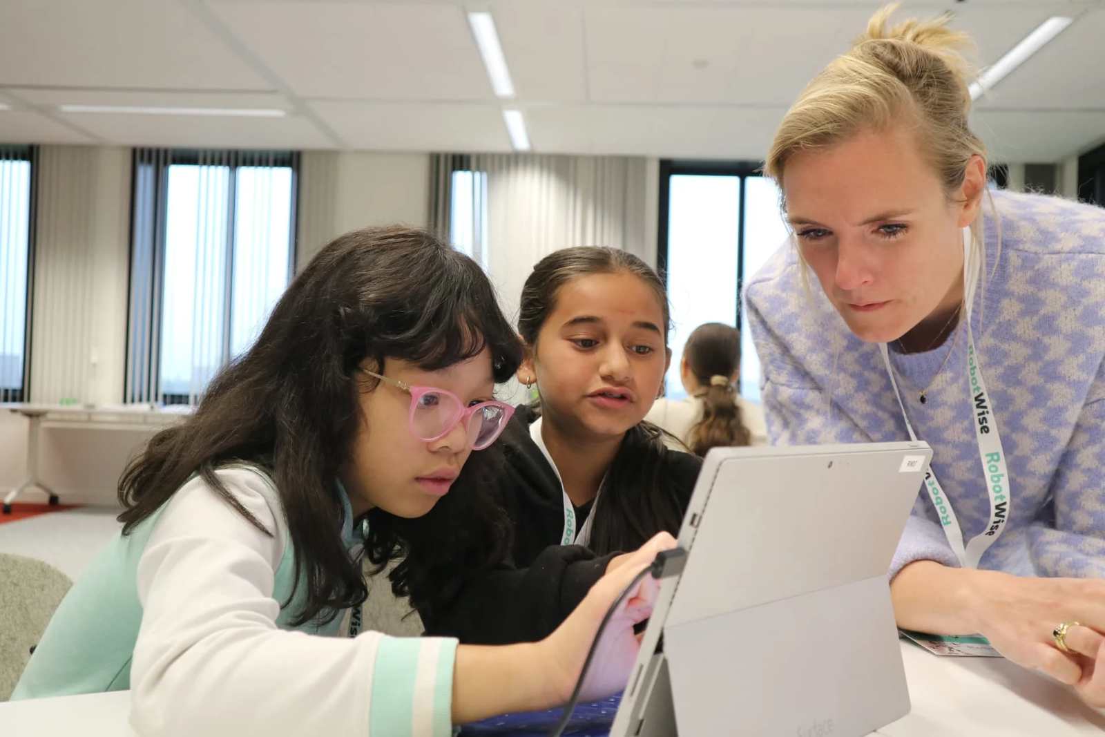 Co-teacher helpt twee leerlingen die samen achter een laptop werken