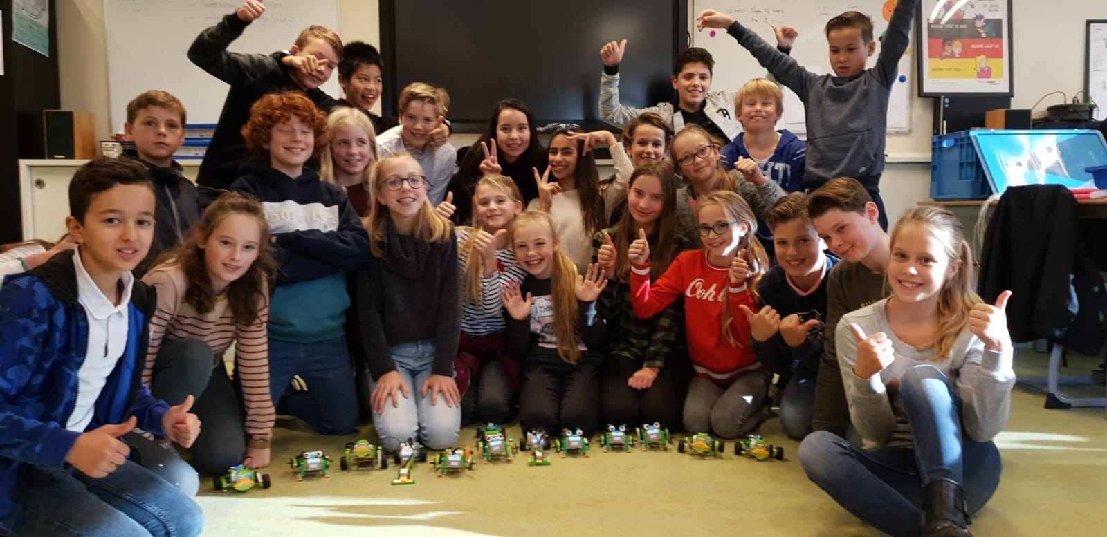 Een enthousiaste schoolklas steekt de duimen op na een gastles met robots